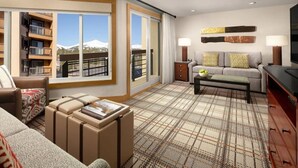 A modern hotel room with a large window offering a mountain view, a cozy seating area with a sofa and ottoman, a flat-screen TV, and a plaid-patterned carpet.