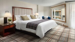 A hotel room with a large bed, two bedside tables with lamps, a window with a view, and a plaid-patterned carpet.