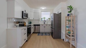 A compact kitchen with white cabinets, stainless steel appliances, and a wooden ladder shelf. - Charming 3BR Beach House with BBQ in Grand Bend (Grand Bend)