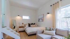 A modern bedroom with a bed, bedside tables, a sofa, a coffee table, and a staircase. - Charming 3BR Beach House with BBQ in Grand Bend (Grand Bend)