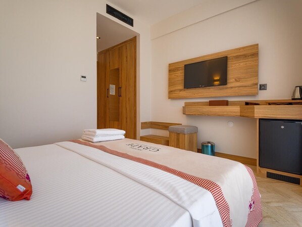 A hotel room with a bed, a TV mounted on the wall, a small desk, and a refrigerator. - GRAPE HOTEL (Ezine)