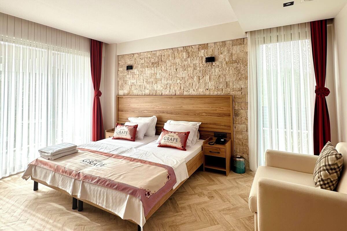 A modern hotel room with a large bed, wooden headboard, and a sofa.