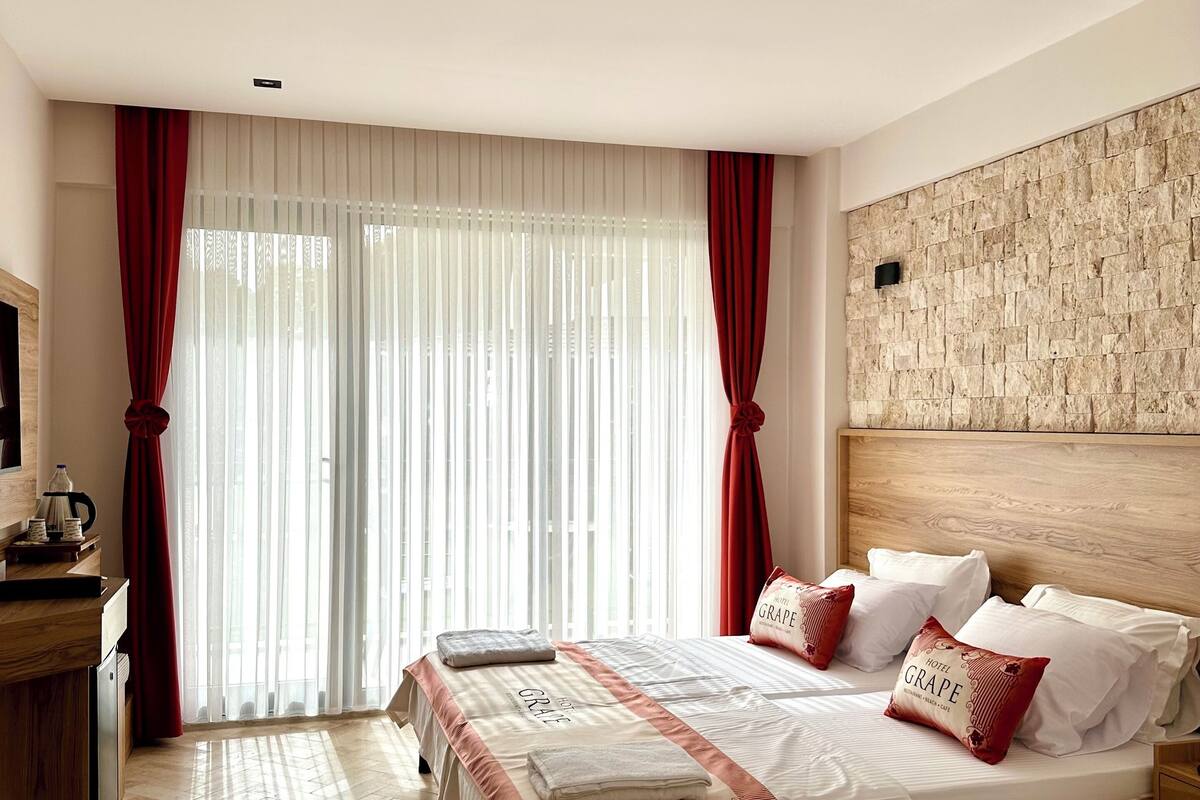 A hotel room with a large bed, wooden headboard, and a stone-textured wall.