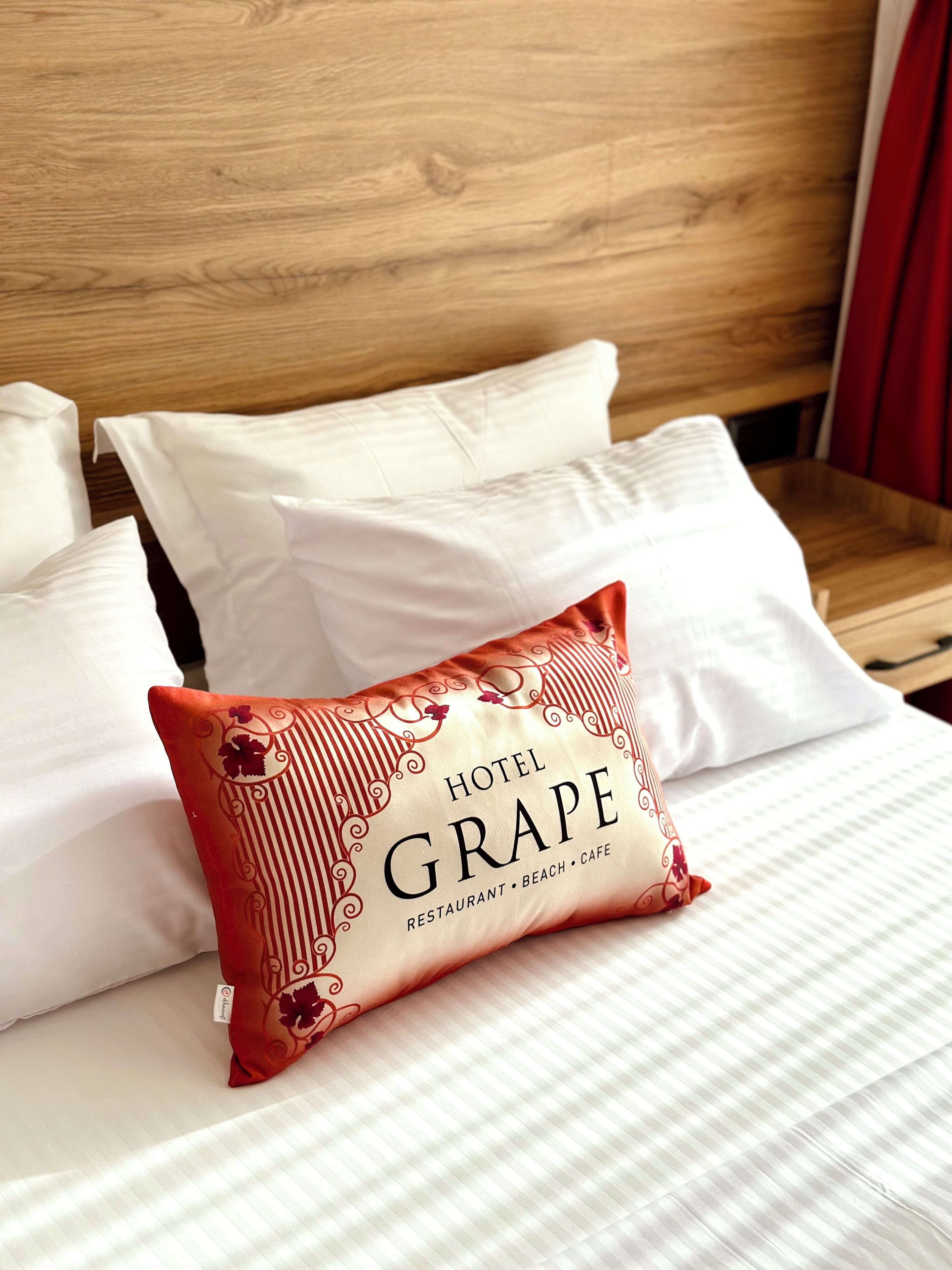 A hotel bed with white bedding and a decorative pillow labeled "Hotel Grape."