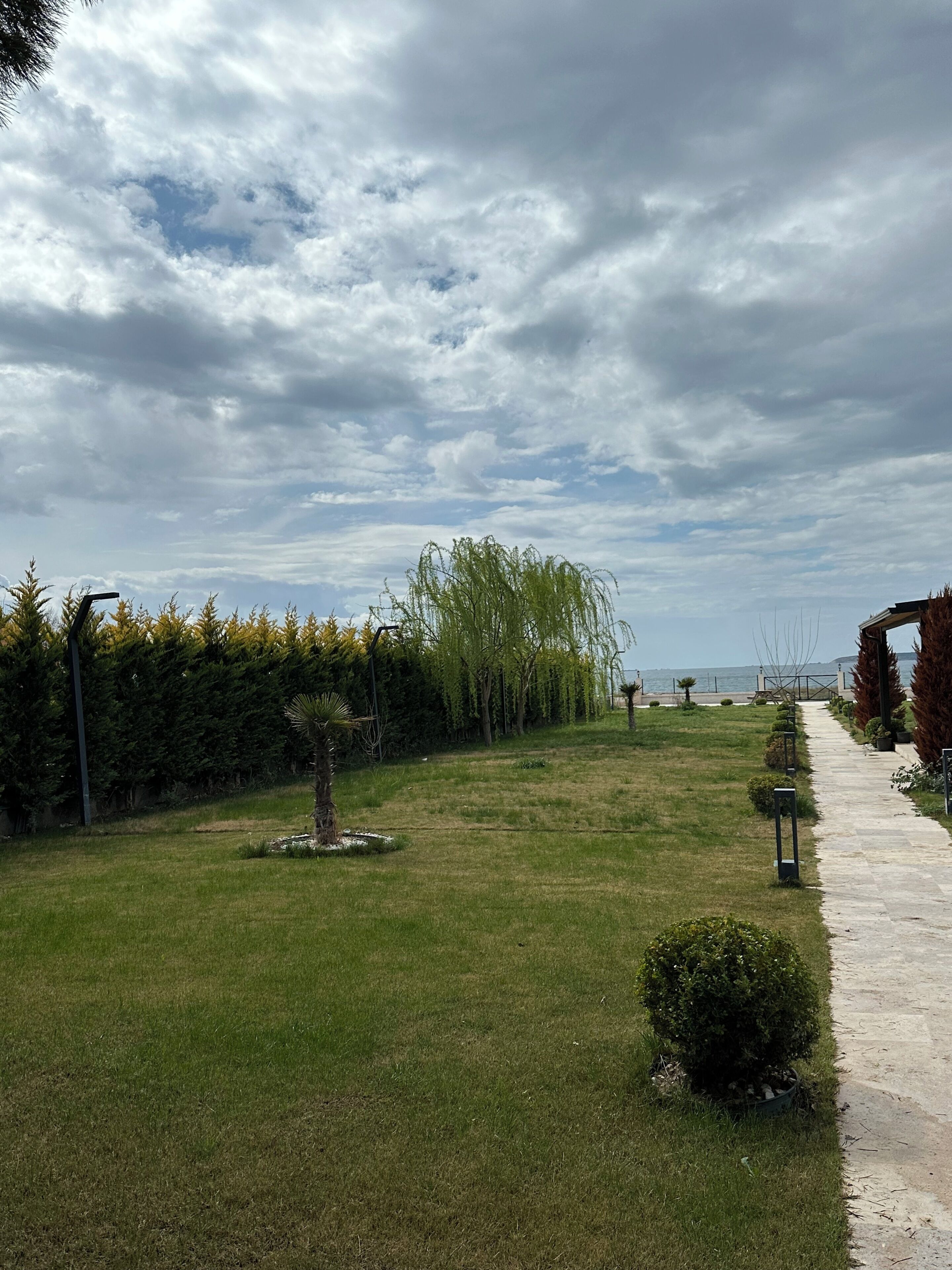 A grassy pathway leading to a building with a view of the sea.