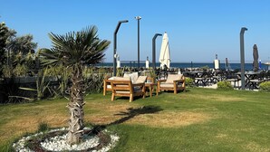 A patio area with outdoor seating, a palm tree, and a view of the sea. - GRAPE HOTEL (Ezine)