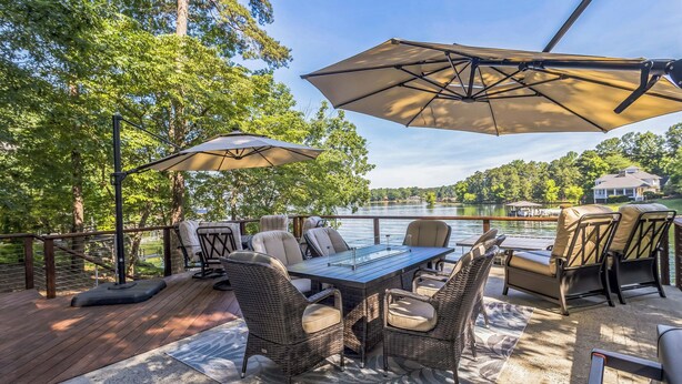 An outdoor deck with a dining table, chairs, and umbrellas, overlooking a lake.