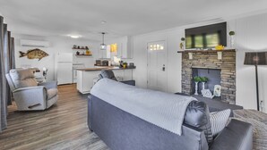 A modern living room with a grey sofa, a dining area with a kitchen in the background, and a fireplace with decorative items.