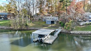 A house with a dock extending into a calm lake, surrounded by trees and a well-maintained lawn.