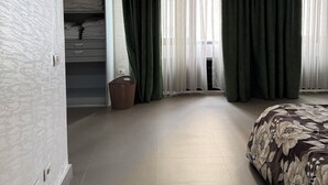 Ein Schlafzimmer mit Bett, Kleiderschrank, Fenster mit Vorhängen und Deckenleuchte.