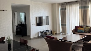 Ein modernes Wohnzimmer mit flachbildfernseher an der Wand, einem Essbereich mit Tisch und Stühlen sowie einer Couch mit Kissen.