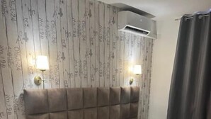 Ein Schlafzimmer mit einem Bett, Nachttischen, einem Wandklimagerät und einem Vorhang.