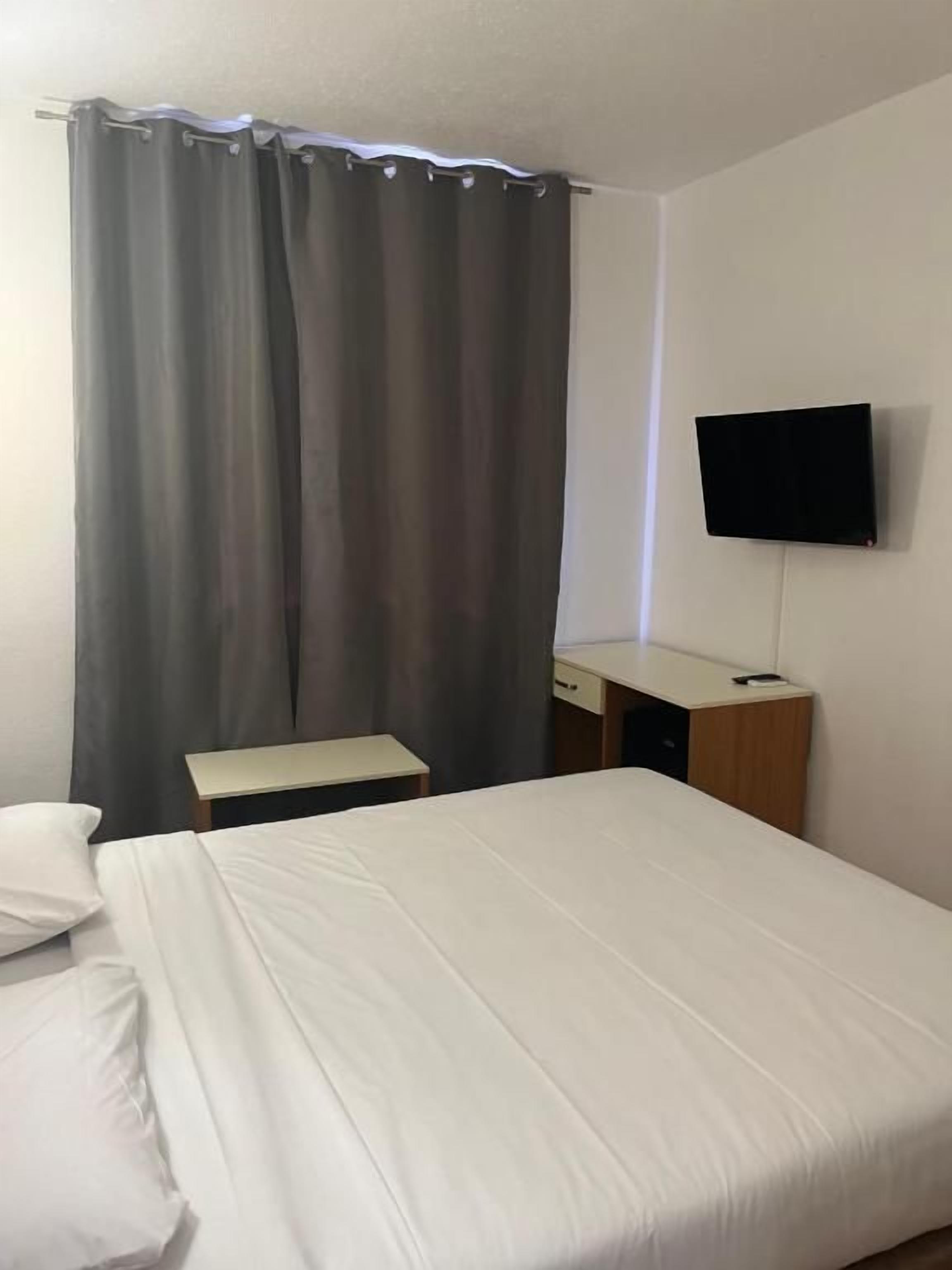 A hotel room with a bed, a desk, a chair, a television, and a curtain.