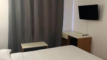 A hotel room with a bed, a desk, a chair, a television, and a curtain.