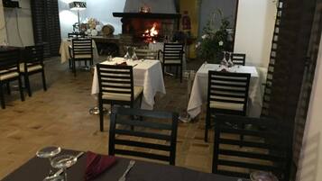 A restaurant with tables set for dining, a fireplace, and a view of the outside.