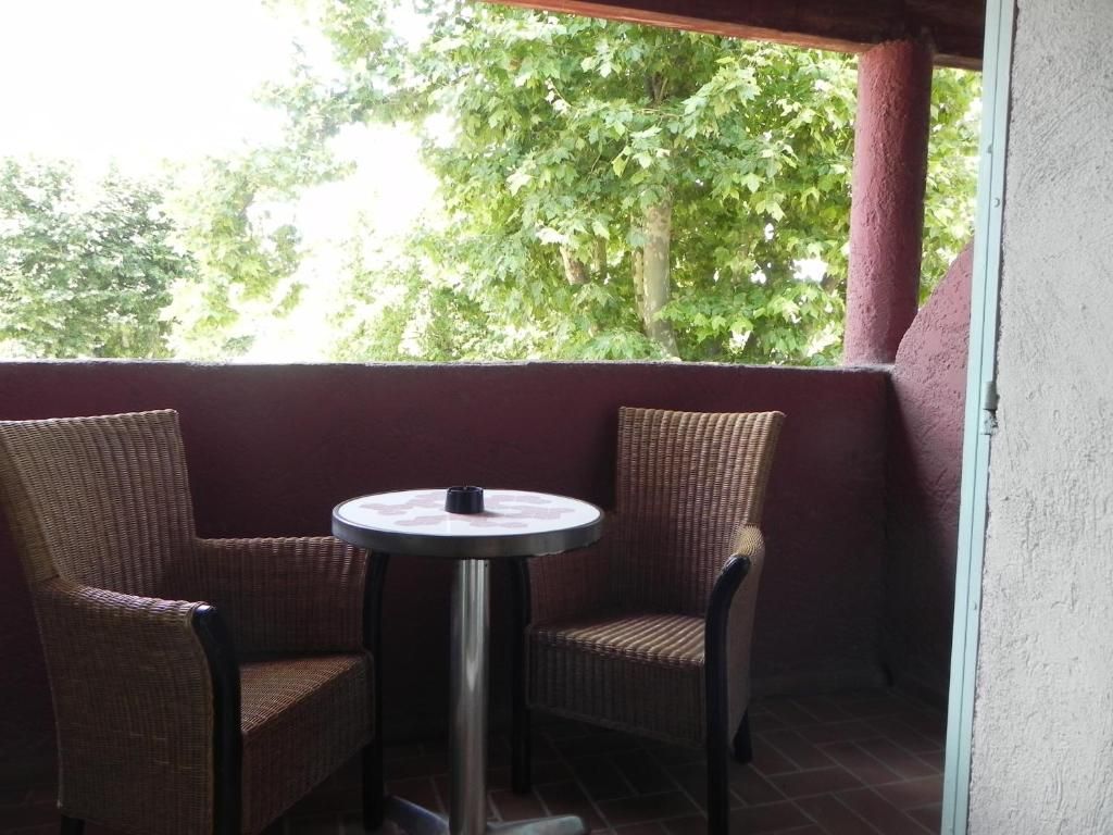 A balcony with wicker chairs and a small round table, overlooking a green area with trees.