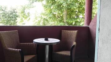 A balcony with wicker chairs and a small round table, overlooking a green area with trees.