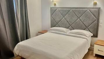 A bedroom with a bed, wooden floor, grey curtains, and two bedside lamps.