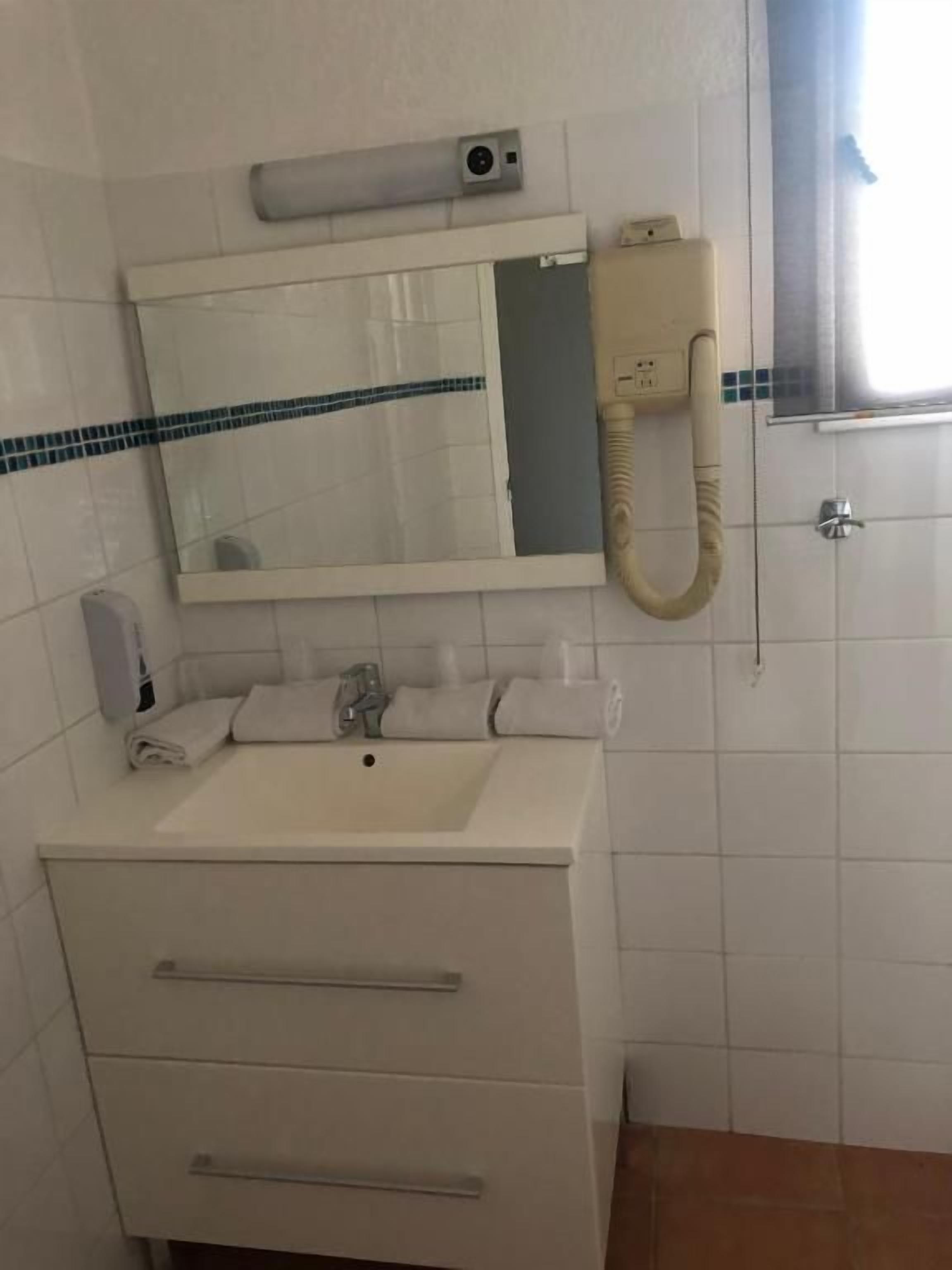 Une salle de bain avec un lavabo blanc, un miroir, un sèche-cheveux et un porte-serviettes.