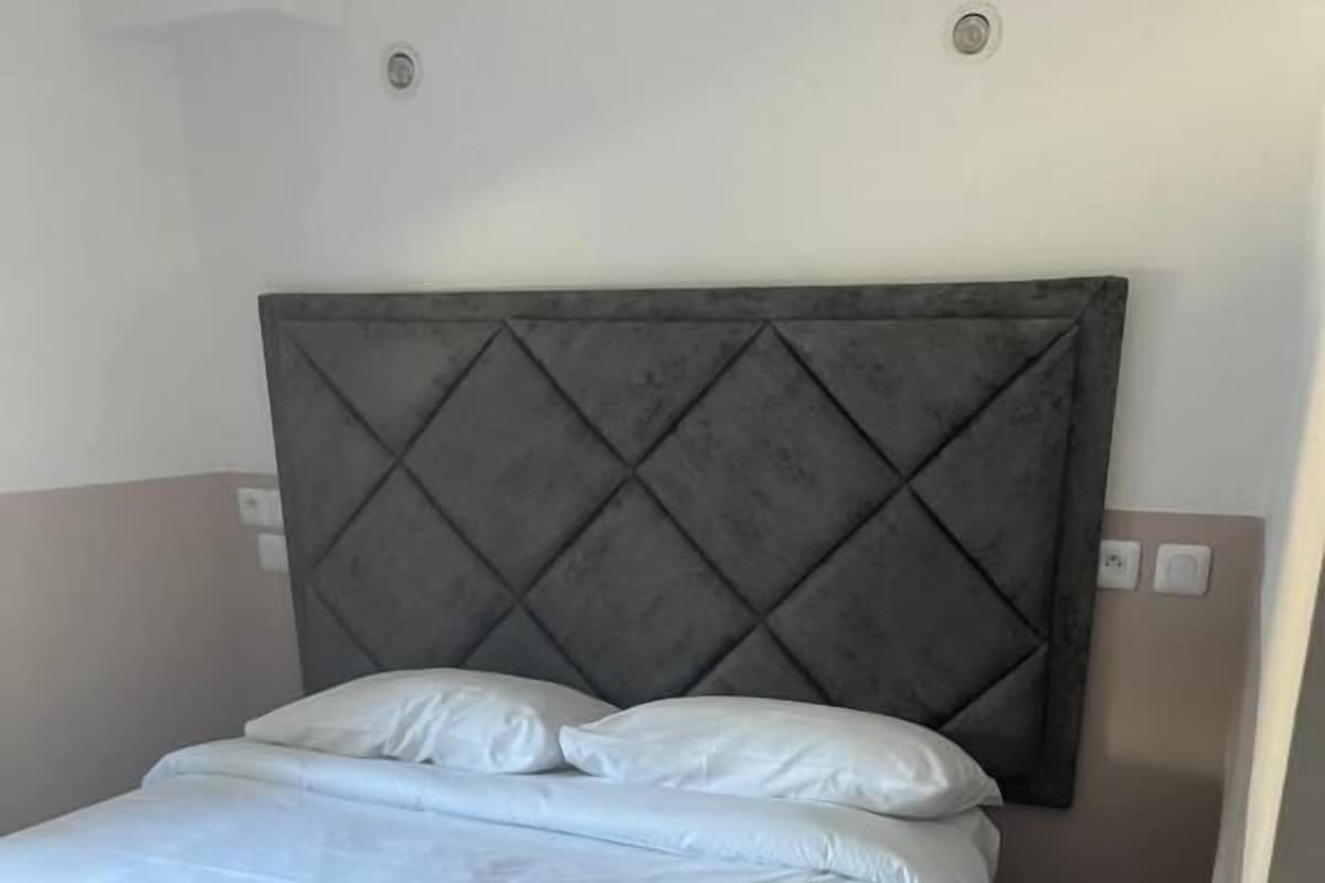 Una cama con cabecera capitonada, ropa de cama blanca y pared en tonos neutros.