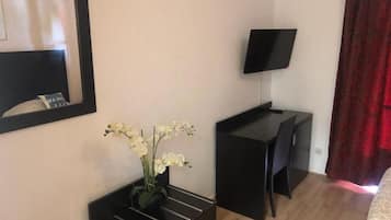 Quarto de hotel com cama, escrivaninha, televisão de tela plana, um vaso com flores e um espelho na parede.