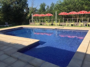 A swimming pool with a tiled edge, surrounded by chairs and red umbrellas.