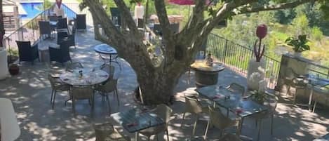 An outdoor patio area with tables and chairs, surrounded by trees.