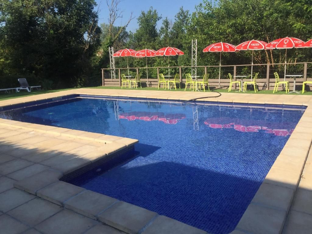 A swimming pool with a tiled edge, surrounded by chairs and red umbrellas.