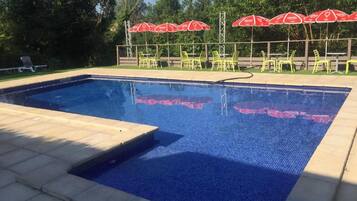 A swimming pool with a tiled edge, surrounded by chairs and red umbrellas.