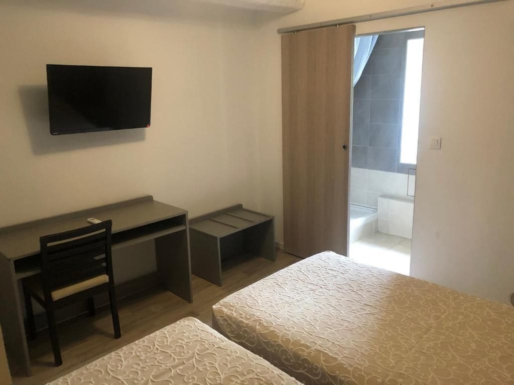 A bedroom with a bed, a desk, a chair, and a TV.