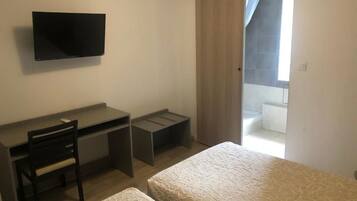 A bedroom with a bed, a desk, a chair, and a TV.