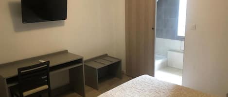 Un dormitorio con cama, escritorio, silla y televisor.