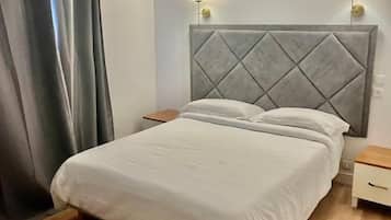 A bedroom with a bed, wooden floor, grey curtains, and two bedside lamps.