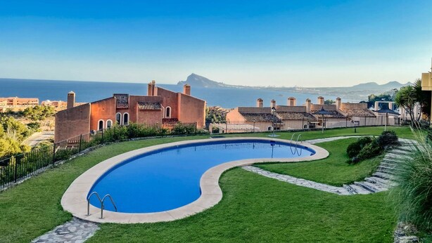 A pool with a curved edge, surrounded by a well-maintained lawn and a stone pathway. - Charming Townhouse with Sea Views & Pool in Altea (Altea)
