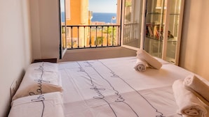 A hotel room with a bed, a window with a view of the sea, and a glass door leading to a balcony. - Charming Townhouse with Sea Views & Pool in Altea (Altea)