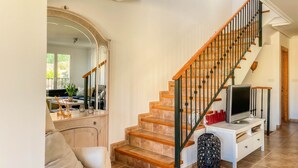 A spacious living room with a wooden staircase, a large mirror, and a television on a white console. - Charming Townhouse with Sea Views & Pool in Altea (Altea)