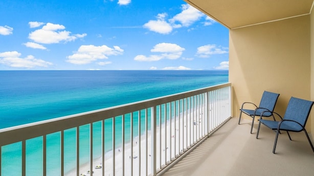 A balcony with a view of the ocean and beach, featuring two chairs and a railing.