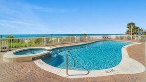 A swimming pool with a hot tub, surrounded by a white fence, and a view of the ocean.