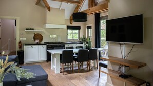 A modern kitchen with white cabinets, a dining table with chairs, a flat-screen TV mounted on the wall, and wooden beams on the ceiling. - Farmhouse in Veluwe With Sauna and Nature Views (Ermelo)