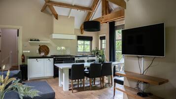 A modern kitchen with white cabinets, a dining table with chairs, a flat-screen TV mounted on the wall, and wooden beams on the ceiling.