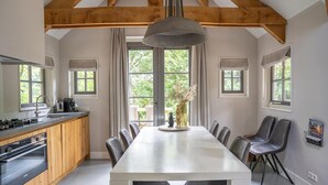 A spacious kitchen with a long island, wooden beams, large windows, and modern appliances. - Farmhouse in Veluwe With Sauna and Nature Views (Ermelo)