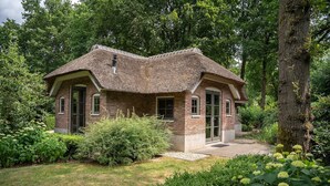 A small brick house with a thatched roof, surrounded by lush greenery and trees. - Farmhouse in Veluwe With Sauna and Nature Views (Ermelo)