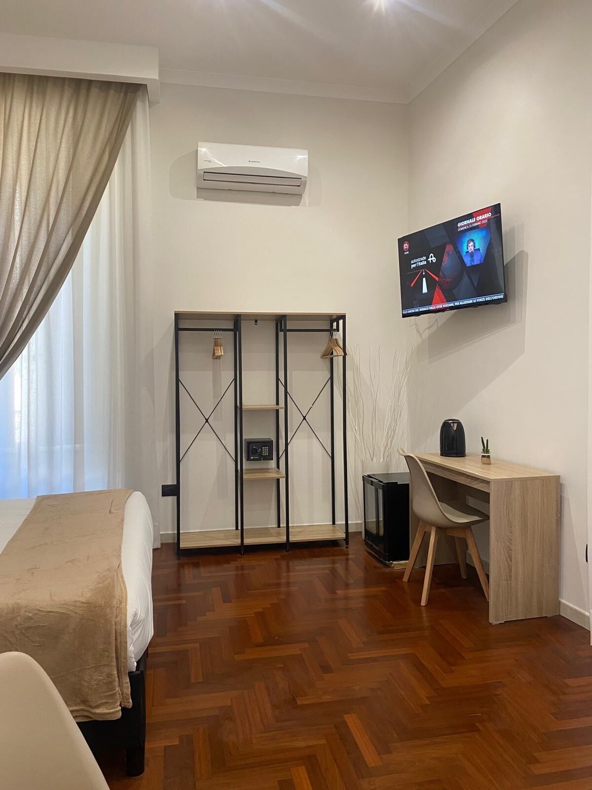 A modern hotel room with a bed, a desk, a TV, and a wardrobe.