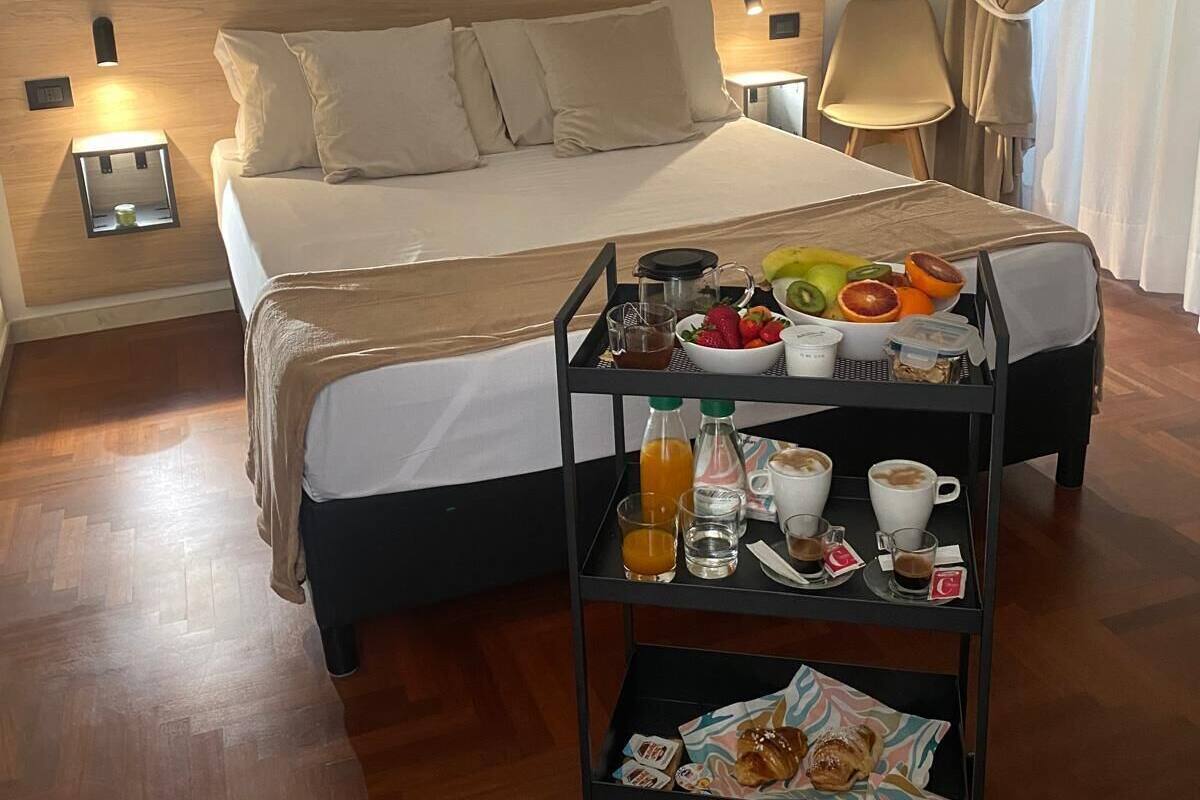 A hotel room with a bed, a breakfast trolley, and a painting on the wall.