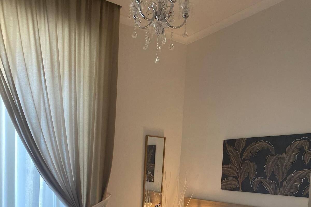 A bedroom with a large bed, a chandelier, a mirror, and a painting on the wall.