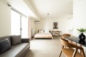 A modern hotel room with a sofa, a bed, a dining table with chairs, and a large window. - Elysee apartment 8 (Athens)
