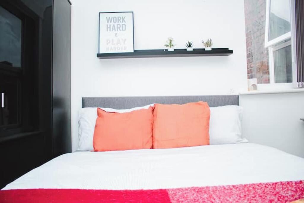 A bedroom with a bed, a pillow, a bedside table, a wall-mounted shelf with small plants, and a motivational quote on the wall.