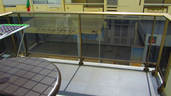 A glass railing with the word "Campidoce" on it, a tiled floor, and a table with a laptop on it.
