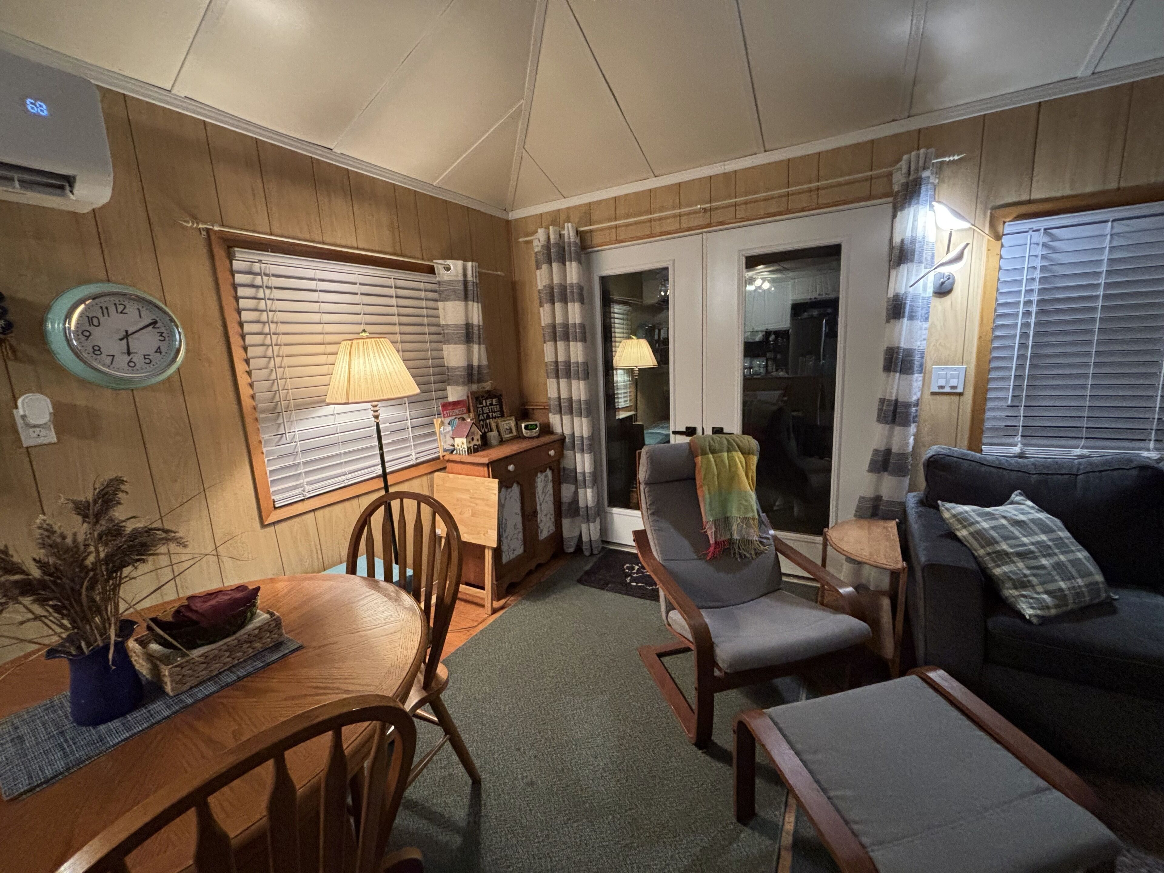 A cozy living room with a wooden floor, a dining table with chairs, a sofa, and a lamp.
