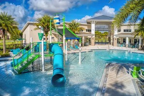 Une piscine avec un toboggan, des palmiers et un bâtiment doté d’une zone couverte en arrière-plan.